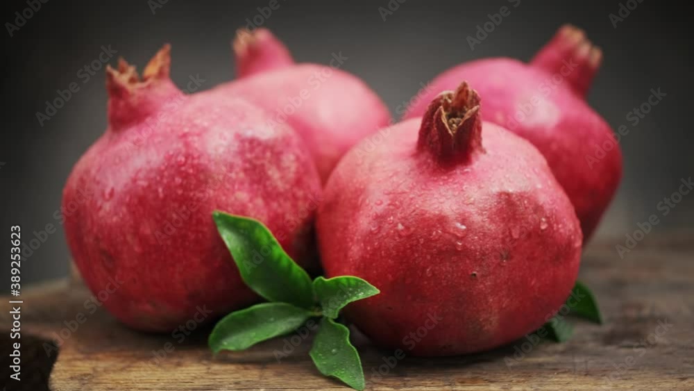 Ripe pomegranate fruits with leaves on a wooden board rotate on its axis on a dark background. Pomegranate fruit. Ripe pomegranate fruits with leaves on a wooden board rotate on its axis on a dark background. Pomegranate fruit.
