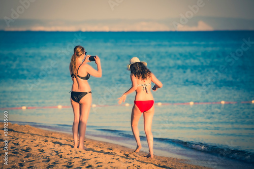 Mother photographing her daughter using smartphone at tropical beach