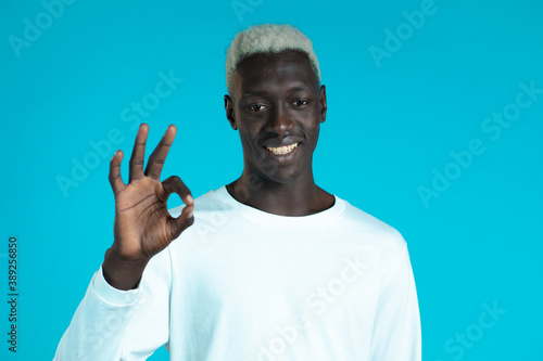 Mixed race man showing thumb up sign over blue background. Positive african guy smiles to camera. Winner. Success. Body language. © kohanova1991
