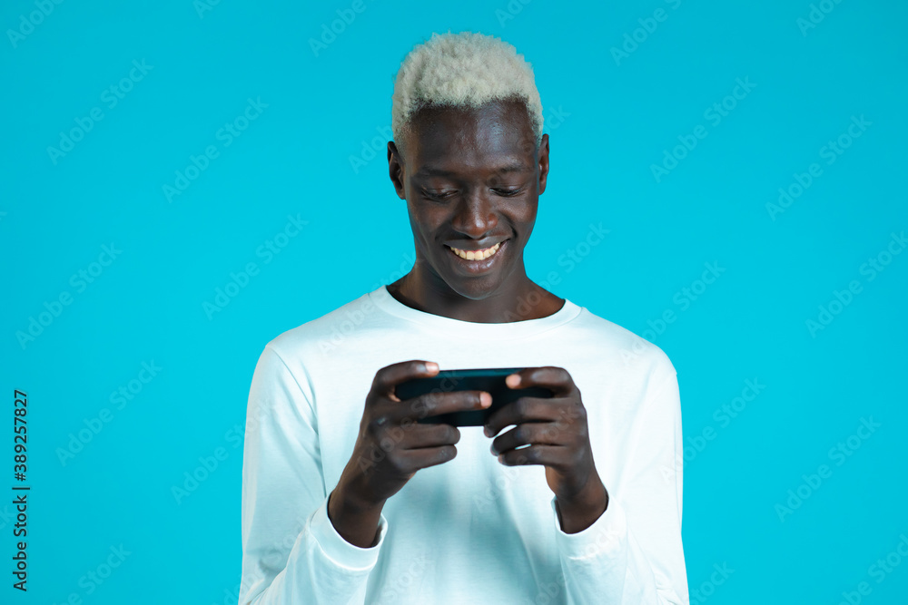Handsome african man playing game on smartphone on blue studio wall. Using modern technology - apps, social networks. Handsome african man playing game on smartphone on blue studio wall. Using modern technology - apps, social networks.