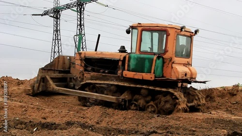 A bulldozer is leveling the ground for construction, in the background of the tower for high voltage wires.