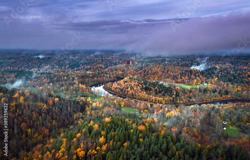 Picturesque valley of colorful trees in Sigulda. Morning mist covering forest and river Gauja. Turaida castle. 