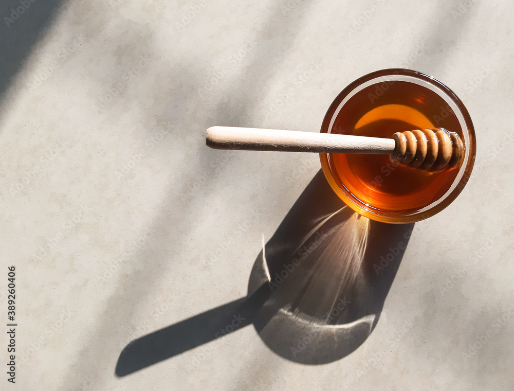 Wooden honey dipper in honey on off-white background in natural sunlight.fresh honey in glass bowl with wooden honey stick. Wooden honey dipper in honey on off-white background in natural sunlight.fresh honey in glass bowl with wooden honey stick.