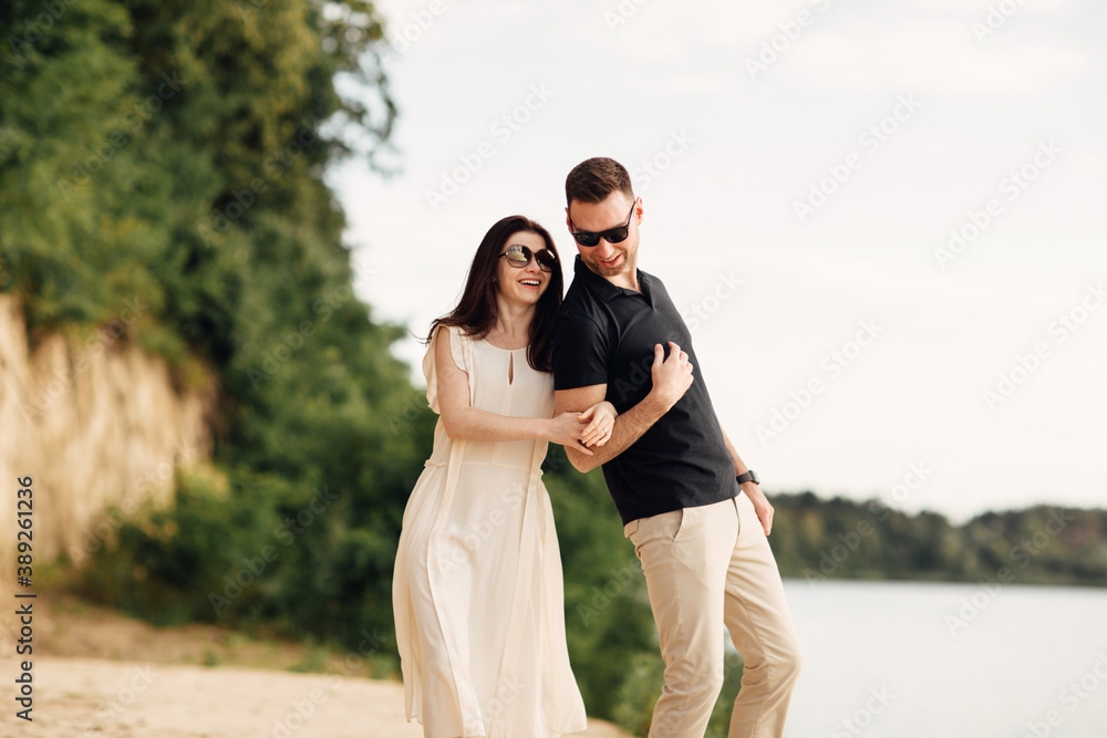 Happy lovers at the beach near lake. Young couple is holding hands and walking on summer day outdoors. A man and woman in love. Concept of love and family. full length. Close Up. Happy lovers at the beach near lake. Young couple is holding hands and walking on summer day outdoors. A man and woman in love. Concept of love and family. full length. Close Up.