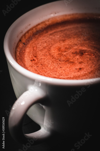 Fotografía vertical de una taza blanca llena de café con espuma cremosa tipo capuccino