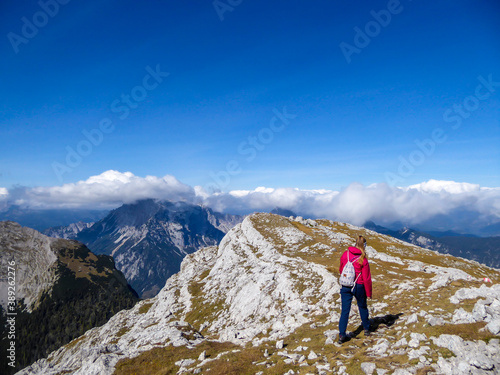 A woman in pink jacket enjoying the Alpine landscape from Hochzin?dl peak in Austria. Steep, sharp mountains around her. Fall landscape - golden grass. Exploring and experiencing the nature