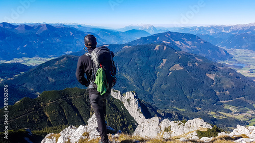 A man in climbing outfit standing at the top of Kaiserau Kreuzkogel in Austrian Alps. He is looking at the endless view in front of him. Panoramic Alps view. Exploring the mountains. Discovering