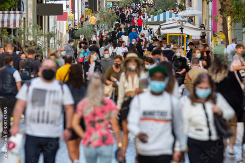 crowd goes up and down a busy shopping street wearing a protective mask