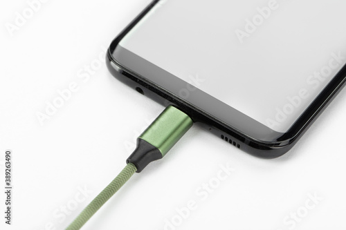 Mobile phone with connected charging cable on a white background.