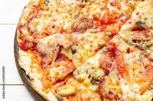 Delicious simple pizza with tomatoes, mozzarella and bacon on white wooden background.