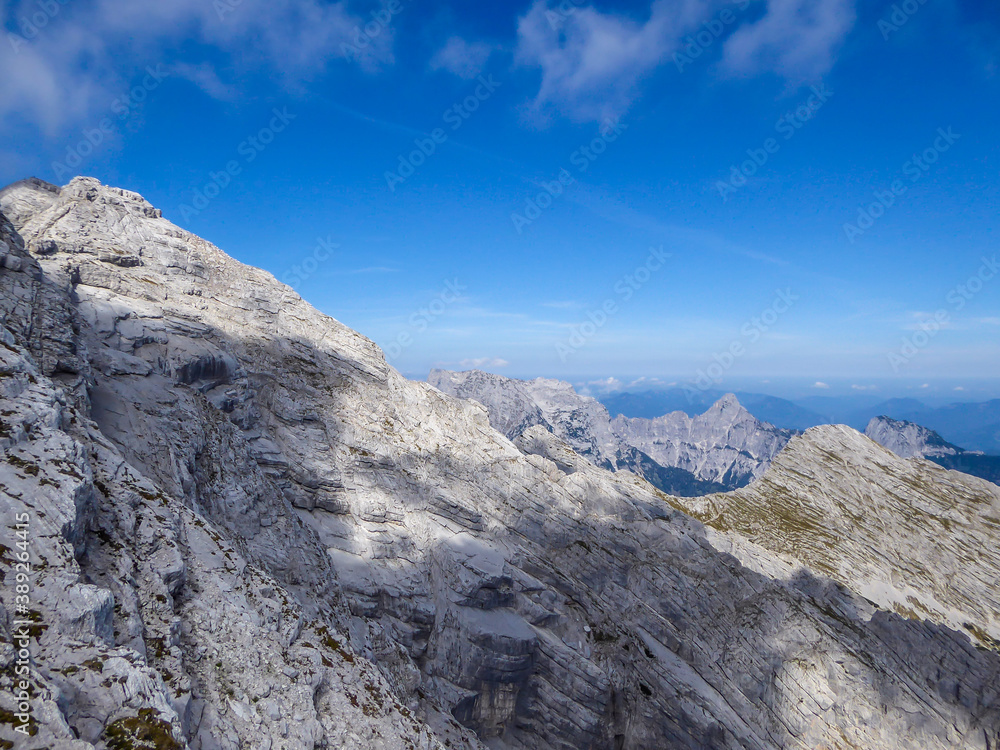A panoramic view on endless mountain chains from top of a mountain in Hochtor region, Austrian Alps. High Alpine mountaineering. Sunny, cloudless summer day. Sharp and stony slopes in the foreground.