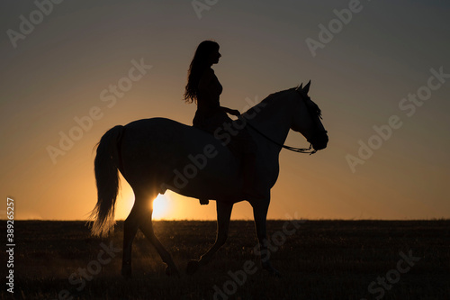 Attractive young Caucasian female with a beautiful dress riding a horse in the countryside at sunset