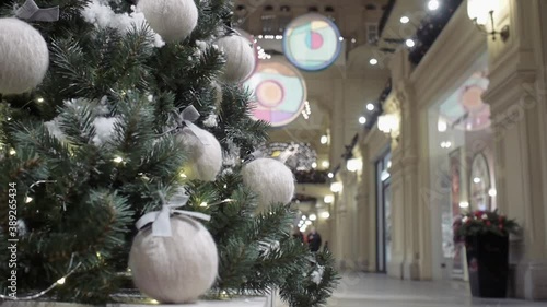 A Christmas tree decorated with woolen balls of thread stands in the lobby of a shopping center against the backdrop of shop windows.