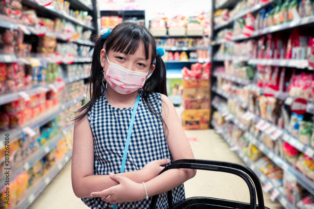 Asian little girl wearing face mask and standing with baskets in the supermarket