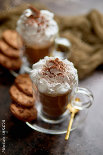 Two tall glasses with hot chocolate, whipped cream and cinnamon powder on top