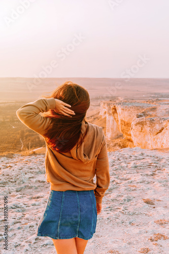 Rear view of a woman holding her long hair and walking on a rocky mountain in an orange sunset  the concept of tourism and freedom