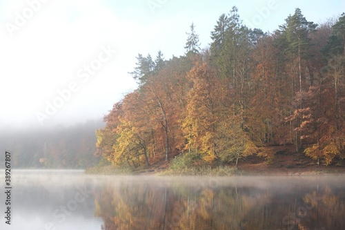 Beautiful landscape with a misty lake and trees in autumn colors and their reflections in water. Otomin Lake  Kashubia  Poland
