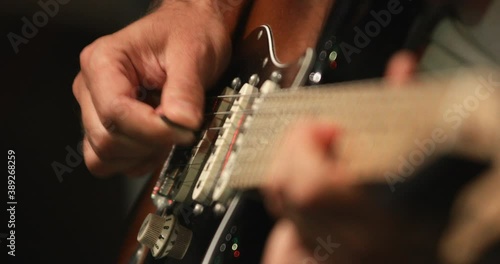 Musician playing solo using electric guitar during recording session, close up at hand and fret-board and focus on right hand in background