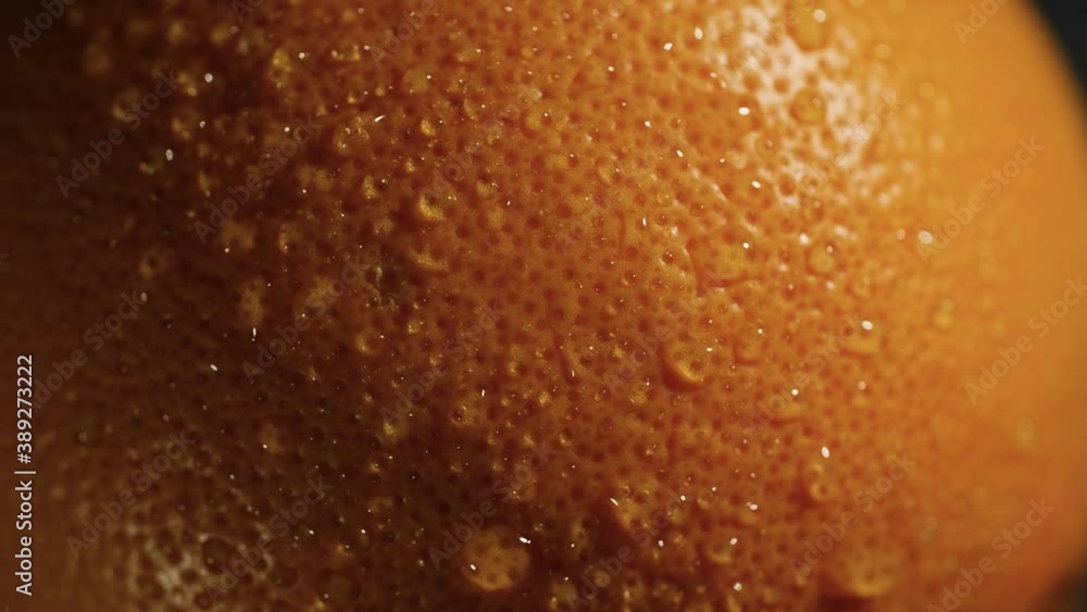 4K Close up of an orange or grapefruit skin with water drops. Rotating macro video of the bright and beautifully textured fresh fruit with high contrast.