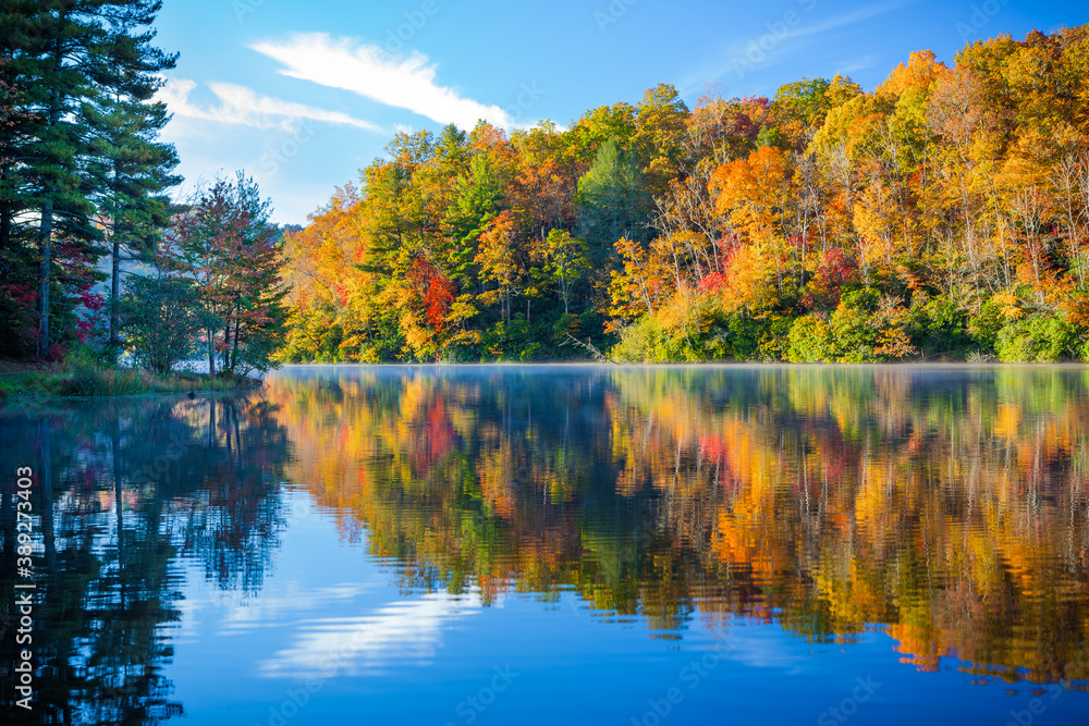 Mist rises over calm lake with autumn colors