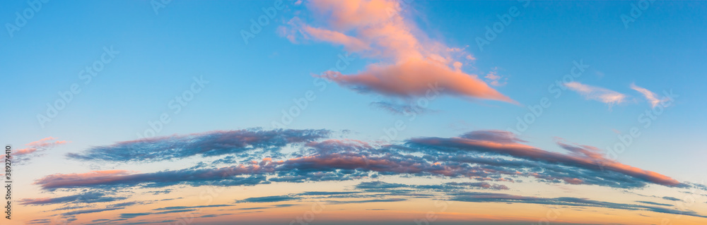 Vanilla sunset sky panoramic shot. Pink golden blue evening sky with long stratus clouds over the horizon. Pastel colored calm skyscape.