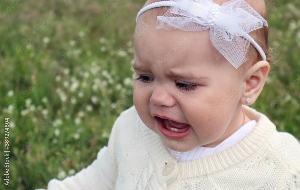 Little girl in a white bandage crying, opening her mouth with two teeth, outdoors, close-up Little girl in a white bandage crying, opening her mouth with two teeth, outdoors, close-up