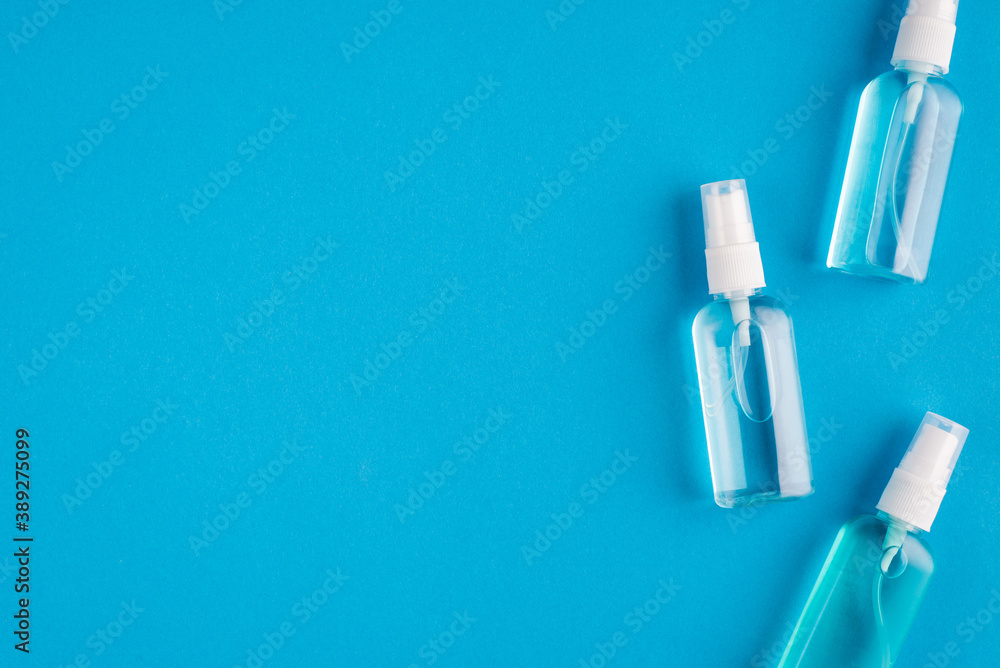 Top above overhead close up view photo of three little bottles with transparent sanitizing liquid isolated over bright color blue background Top above overhead close up view photo of three little bottles with transparent sanitizing liquid isolated over bright color blue background