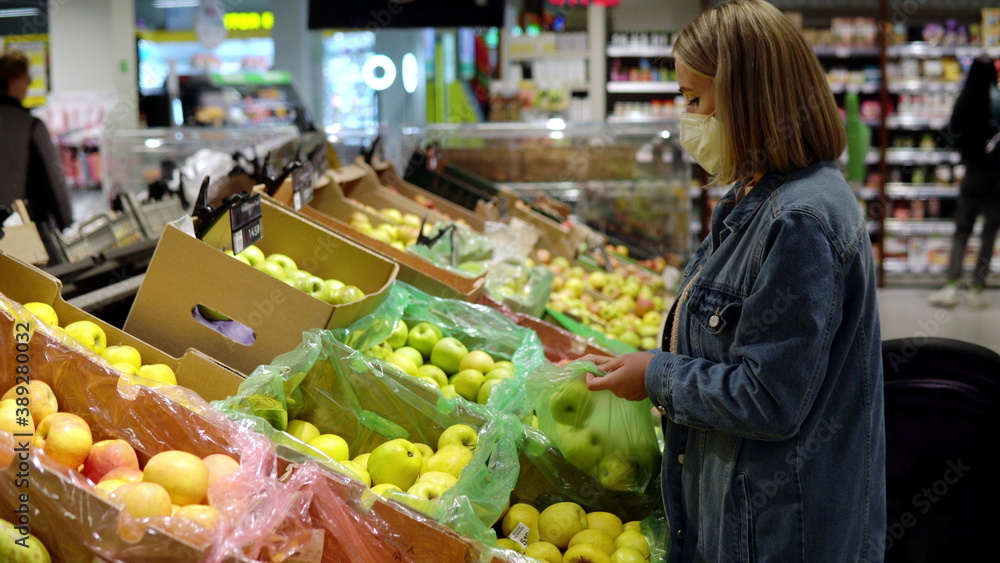 Young woman in mask picks apples in a bag in a store