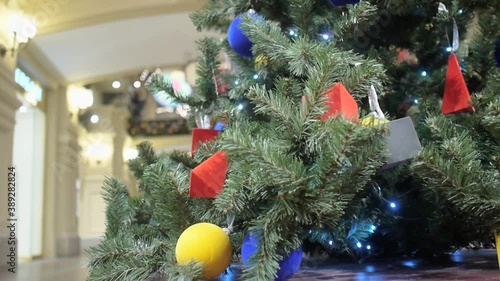 Christmas tree decorated with bright geometric toys stands in the aisle of the GUM shopping center. Visitors pass by out of focus