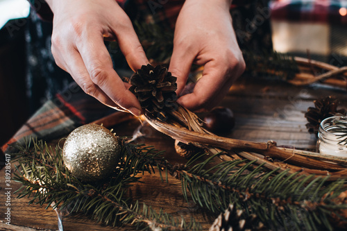 Making of Christmas wreath from nature materials on a dark wooden table. Scandinavian hygge styled Christmas composition. Cozy winter homely scene with decorations.