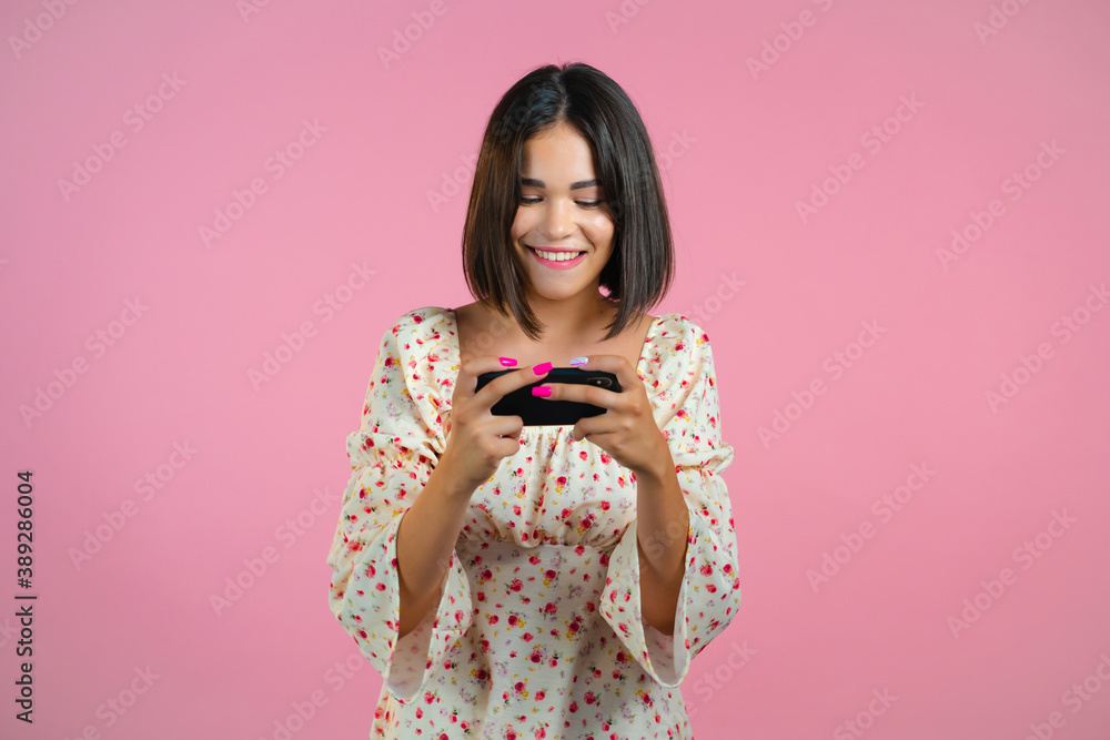 Woman playing game on smartphone on pink studio wall. Using modern technology - apps, social networks. Woman playing game on smartphone on pink studio wall. Using modern technology - apps, social networks.