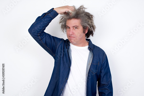 Handsome mature caucasian man with afro grey hair standing over white background saying: Oops, what did I do? holding hand on head with frightened and regret expression.