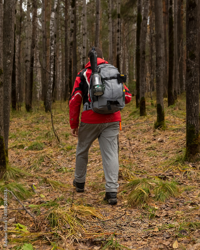 Young man in hiking clothes with a backpack, a hatchet and a lantern in the autumn forest. Tourism, activity, lifestyle.