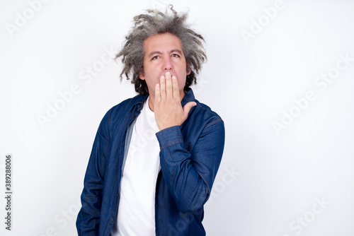 Oh! I think I said it! Close up portrait of gentleman in white, street style t-shirt cover open mouth by hand palm, look at camera with big eyes isolated on bright gray background.