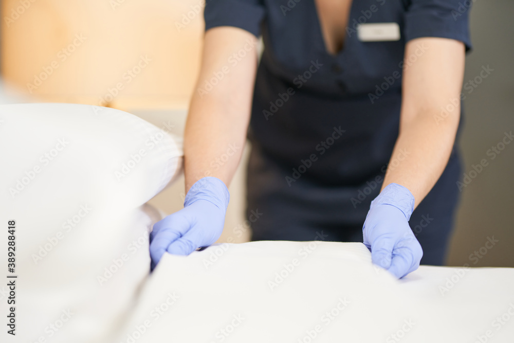 Obraz premium Young housemaid in uniform changing bedding in hotel room