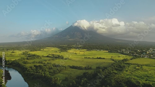 Tropic river with green banks at Mayon volcano eruption aerial. Greenery meadow at fog haze of Philippines mountain at Legazpi town. Rurar fields at stream. Filipino tourist landmark at countryside photo