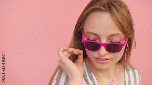 Young caucasian woman with sunglasses listening to the music using headphones . Isolated on pink background, close up. High quality photo