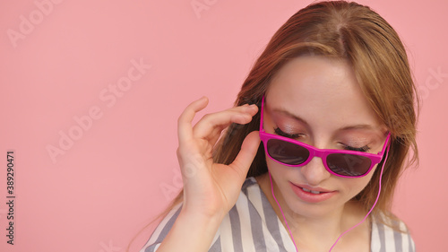 Young caucasian woman with sunglasses listening to the music using headphones . Isolated on pink background, close up. High quality photo