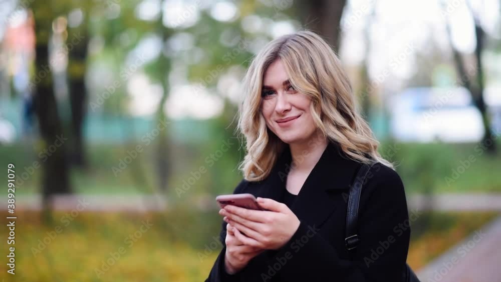 Pretty girl standing with phone and smiling looking up at camera Pretty girl standing with phone and smiling looking up at camera