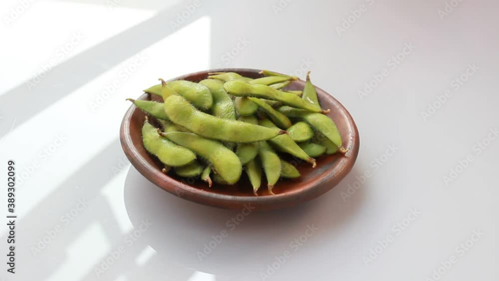 peas in a bowl. Edamame is a preparation of immature soybeans in the pod, found in cuisines with origins in East Asia. The pods are boiled or steamed and served with salt or other condiments peas in a bowl. Edamame is a preparation of immature soybeans in the pod, found in cuisines with origins in East Asia. The pods are boiled or steamed and served with salt or other condiments