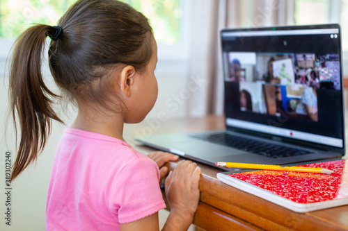 A little kid learning online at home school, video class call, book and pencil. photo