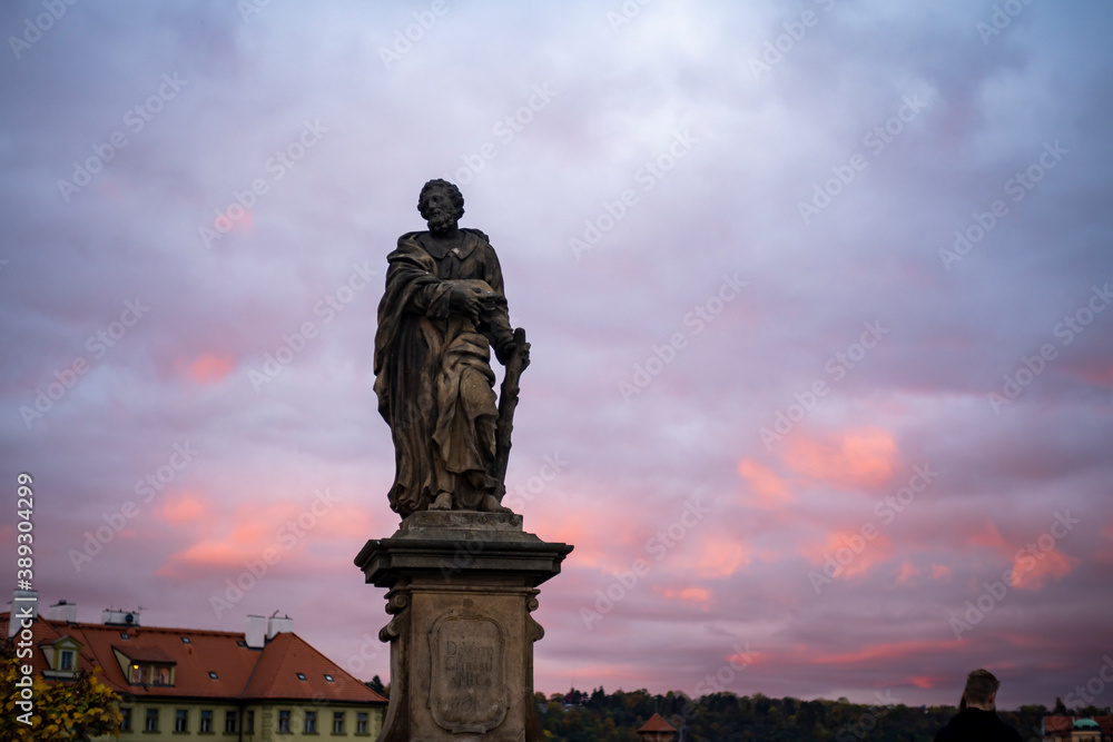 
statue on Charles bridge from 24 century and in the background colorful sky at sunset