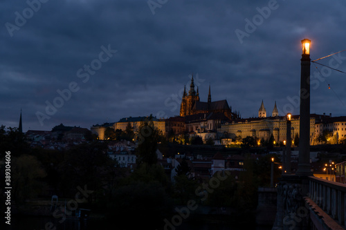  railings and sidewalk for pedestrians and street lights and in the background Prague Castle and St. Vitus Cathedral at night in the center of Prague