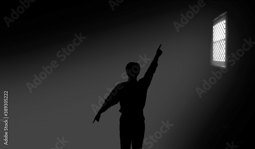Shot of a man with hands stretched out like some clock hands and pointing the window light direction in a small dark room. © mirzamlk