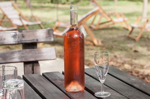 Bottle of rose wine standing on a vintage wooden rustic table next to an empty glass. Rose is a type of wine  close to red