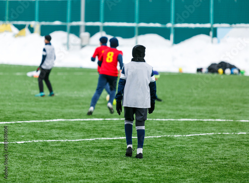 Boys in red sportswear running on soccer field with snow on background. Young footballers dribble and kick football ball in game. Training, active lifestyle, sport, children winter activity © Natali