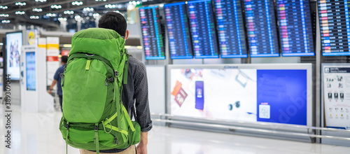 Canvas Print Young man traveler with backpack checking flight time, Asian passenger with hat looking to information board in international airport terminal