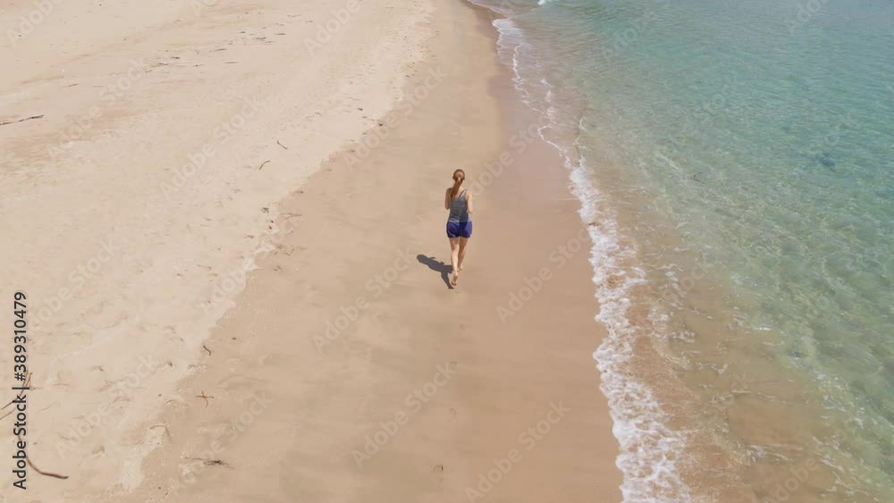 Slowmotion Aerial shot of a young woman running on a beautiful beach. Concept of healthy lifestyle and sports Slowmotion Aerial shot of a young woman running on a beautiful beach. Concept of healthy lifestyle and sports
