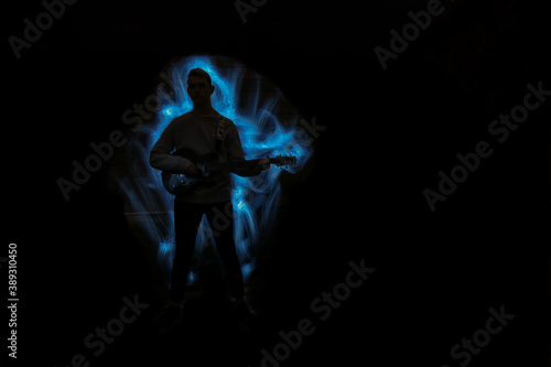 Silhouette of a man with a guitar. Lightpainting scene with a musical instrument and lighting effects in the background.