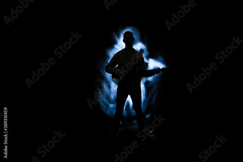 Silhouette of a man with a guitar. Lightpainting scene with a musical instrument and lighting effects in the background.